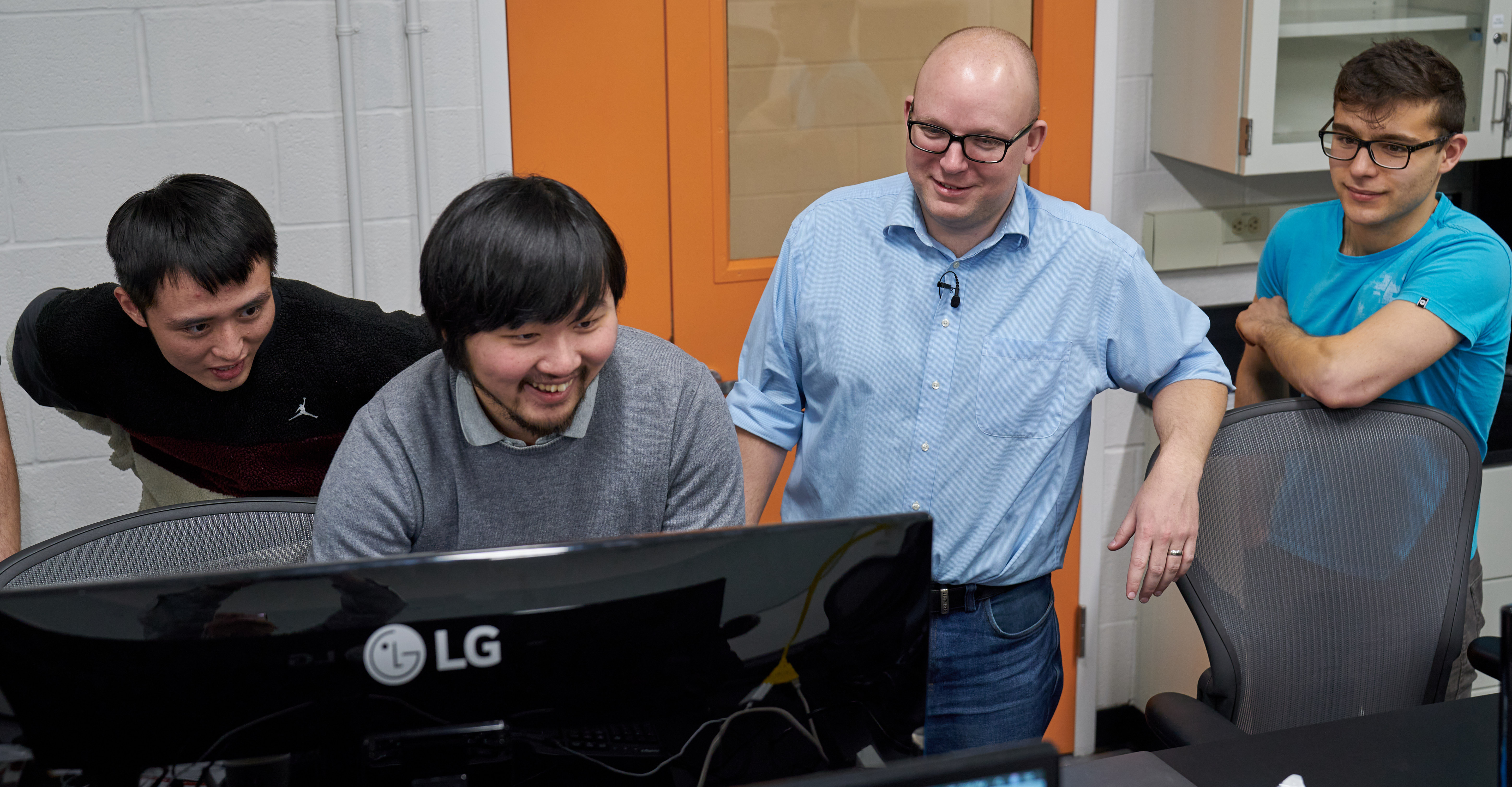 lab members and peter mcmahon gather around a computer laughing 
