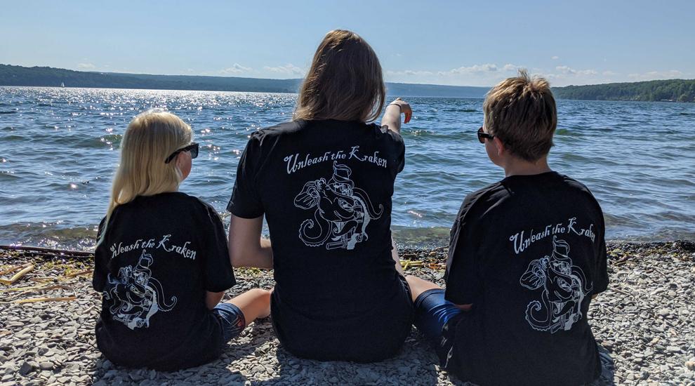 Lena and her children sitting on the sand and looking out over Cayuga Lake.